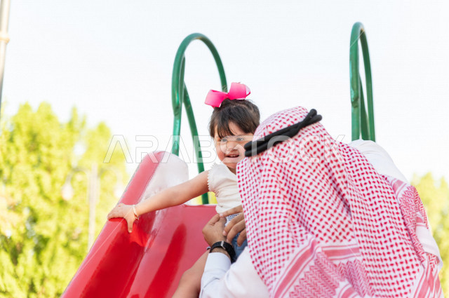 فتاه جميلة مصابة بملازمة داون تقضي وقتها في نزهه مع والدها بالمنتزه ، اب سعودي خليجي يلعب مع ابنته في الهواء الطلق ،تنزلق وتتأرجح في الحديقة في يوم مشمس  ، أصحاب الهمم ، ذوي الاحتياجات الخاصة