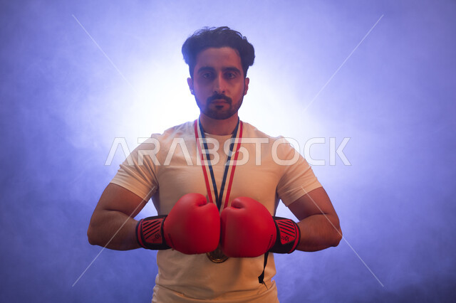 The Saudi National Wrestling Team, physical activity to maintain health and physical fitness, a close-up photo of a Gulf man wearing boxing gloves and a gold medal, practicing combat movements, standing confidently and looking at the camera, discharging n