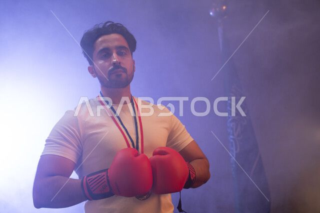 The Saudi National Wrestling Team, physical activity to maintain health and physical fitness, a close-up photo of a Gulf man wearing boxing gloves and a gold medal, practicing combat movements, standing confidently and looking at the camera, discharging n