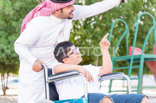 ولد جميل سعوي خليجي مصاب بملازمة داون يقضي وقته في نزهه مع والده  بالمنتزه ، طفل مقعد على كرسي متحرك يستمتع بالهواء الطلق ، أصحاب الهمم ، ذوي الاحتياجات الخاصة ، اعاقة حركية