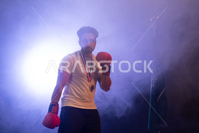 Practicing self-defense, the Saudi national wrestling team, physical activity to maintain health and physical fitness, a Saudi Gulf Arab man wearing boxing gloves and a gold medal, practicing combat movements, discharging negative energy, a blurry backgro