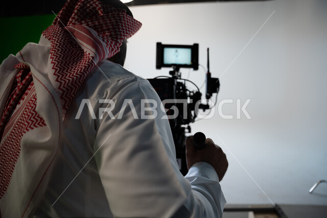 Practicing the hobby of taking pictures with high-resolution cameras, the talent and professionalism of photography, a close-up portrait of a Saudi Gulf Arab man wearing a traditional dress and shemagh, holding a camera, taking souvenir pictures, white ba
