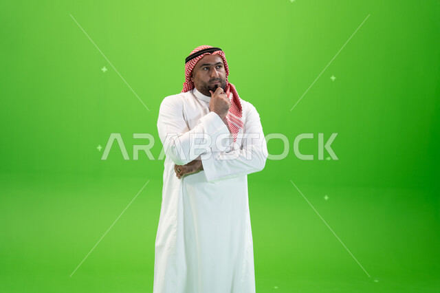 التمعن والتركيز،  التأمل والتخطيط للمستقبل، إيجاد حل لمشكلة ما، رجل عربي خليجي سعودي يرتدي الثوب والشماغ التقليدي يضع يده على ذقنه و ينظر إلى شيء ما بإيماءات التفكير، خلفية خضراء، كروما