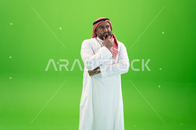 التخطيط للمستقبل والتأمل، إيجاد حل لمشكلة ما، لرجل عربي خليجي سعودي يرتدي الثوب والشماغ التقليدي يضع يده على ذقنه و ينظر إلى شيء ما بإيماءات التفكير، التمعن والتركيز، خلفية خضراء، كروما