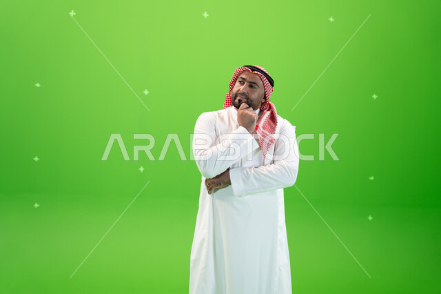 التأمل والتخطيط للمستقبل، إيجاد حل لمشكلة ما، بورتريه مقرب لرجل عربي خليجي سعودي يرتدي الثوب والشماغ التقليدي يضع يده على ذقنه و ينظر إلى شيء ما بإيماءات التفكير، التمعن والتركيز، خلفية خضراء، كروما