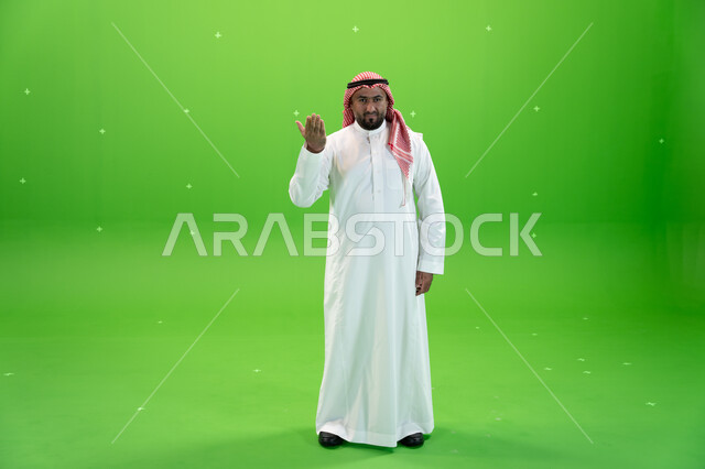 حركات يدين تدل على التوبيخ، طلب التوقف عن فعل الأخطاء، رجل عربي خليجي سعودي يرتدي الثوب والشماغ التقليدي يرفع يده الى الأعلى بإيماءات الغضب، صورة الجسم بالطول الكامل، خلفية خضراء، كروما