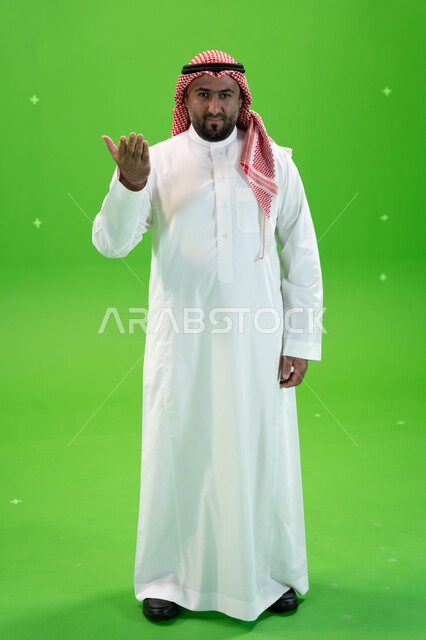 طلب التوقف عن فعل الأخطاء، حركات يدين تدل على التوبيخ، رجل عربي خليجي سعودي يرتدي الثوب والشماغ التقليدي يرفع يده الى الأعلى بإيماءات الغضب، صورة الجسم بالطول الكامل، خلفية خضراء، كروما