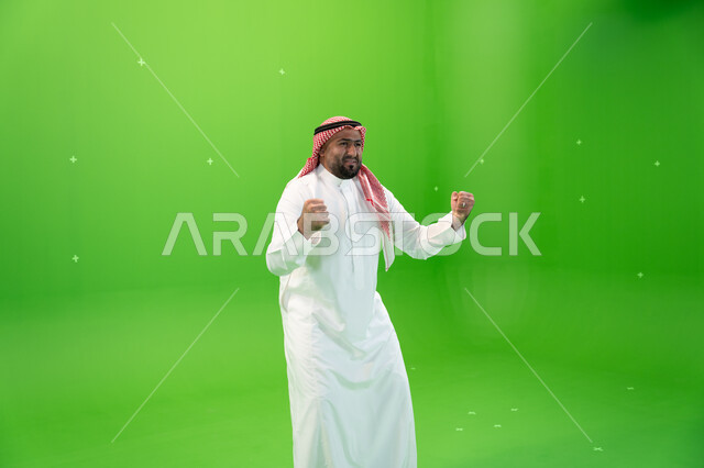 الرضا و الإعجاب و الشعور بالسعاده، تحقيق الاهداف و إنجاز المهامات ,بورتريه لرجل عربي خليجي سعودي يرتدي الثوب والشماغ التقليدي و يرفع يديه فرحا بالنصر, ايماءات تدل على الفوز و الكسب, علامة الفرح والقوه, خلفية خضراء، كروما