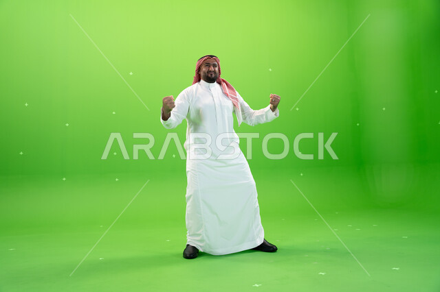 تحقيق الاهداف و إنجاز المهامات ,بورتريه  لرجل عربي خليجي سعودي يرتدي الثوب والشماغ التقليدي و يرفع يديه فرحا بالنصر, ايماءات تدل على الفوز و الكسب, علامة الفرح والقوه, الإعجاب والرضا و الشعور بالسعاده، صورة الجسم بالطول الكامل، خلفية خضراء، كروما