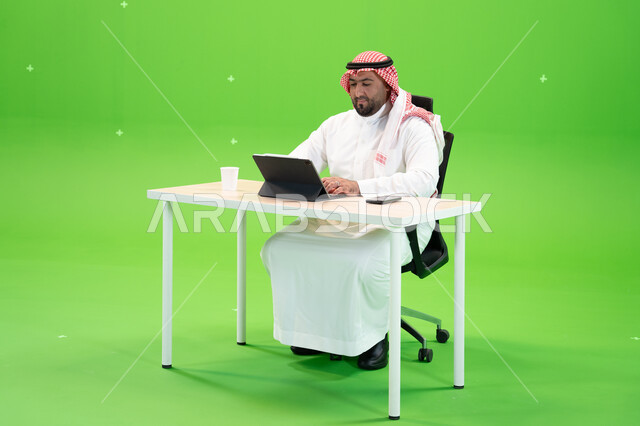العمل في المجال المكتبي, الاجتهاد في تطوير استراتيجة العمل, بورتريه مقرب لرجل أعمال عربي سعودي خليجي يرتدي الزي التقليدي يجلس في مكتبه أمام التابليت, استخدام التطبيقات الالكترونية في المكاتب والوظائف السعودية, الخلفية خضراء, كروما.