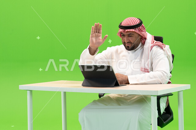إيماءات يدين تدل على السلام والترحيب، القيام بمحادثات عبر الانترنت, إجراء مقابلات عمل أونلاين, استخدام الأجهزة والتقنيات الحديثة, بورتريه لموظف عربي سعودي خليجي يرتدي الزي التقليدي السعودي يقوم بالعمل داخل مكتبه, مهن ووظائف سعودية, خلفية خضراء, كروما. 
