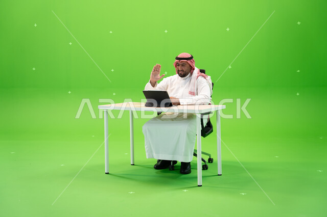 إيماءات يدين تدل على السلام والترحيب، القيام بمحادثات عبر الانترنت, إجراء مقابلات عمل أونلاين, استخدام الأجهزة والتقنيات الحديثة, بورتريه لموظف عربي سعودي خليجي يرتدي الزي التقليدي السعودي يقوم بالعمل داخل مكتبه, مهن ووظائف سعودية, خلفية خضراء, كروما. 