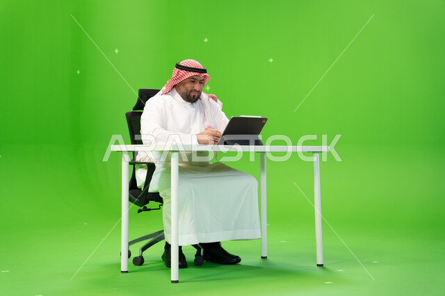 Conducting video chats over the Internet, conducting job interviews online, using modern devices and technologies, a portrait of a Saudi Gulf Arab employee wearing traditional Saudi clothing working inside his office, Saudi professions and jobs, diligence