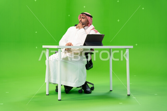 Developing a work plan and mechanism, completing office work, a portrait of a Saudi Arabian Gulf employee wearing the traditional thobe and shemagh doing work in his office, following up administrative affairs with thinking and planning gestures, Saudi pr