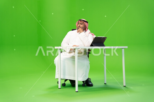تطوير خطة وآلية العمل, إنجاز الأعمال المكتبية, بورتريه لموظف عربي سعودي خليجي يرتدي الثوب والشماغ التقليدي يقوم بالعمل داخل مكتبه, متابعة الشؤون الإدارية بإيماءات التفكير والتخطيط, مهن ووظائف سعودية, خلفية خضراء, كروما.