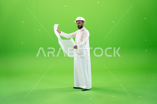 الحرف والمهن السعودية, إدارة المهام والمشاريع الهندسية, التدقيق في مخطط الانشاءات, بورتريه لمهندس عربي خليجي سعودي يرتدي الثوب التقليدي وخوذة الحماية في موقع العمل, صورة الجسم بالطول الكامل, خلفية خضراء, كروما