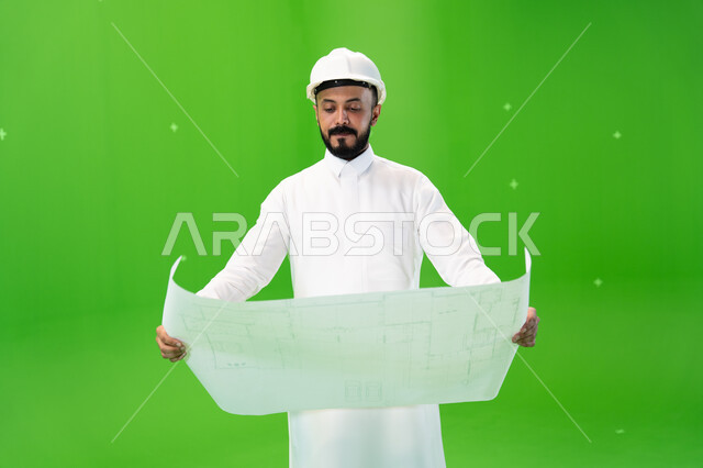 وظائف ومهن سعودية, النظر إلى مخطط الإنشاءات, بورتريه لمهندس عربي خليجي سعودي يرتدي الثوب التقليدي وقبعة الحماية في موقع العمل, مفهوم الهندسة وأعمال البناء, تنمية وتطوير المجال الهندسي السعودي, متابعة الأعمال الهندسية, خلفية خضراء, كروما