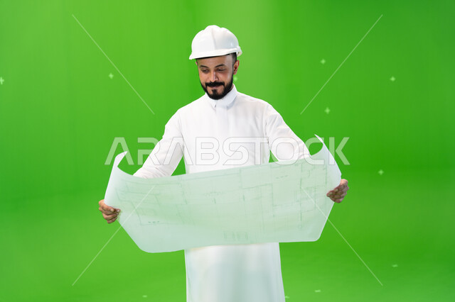 متابعة الأعمال الهندسية, النظر إلى مخطط الإنشاءات, بورتريه لمهندس عربي خليجي سعودي يرتدي الثوب التقليدي وقبعة الحماية في موقع العمل, مفهوم الهندسة وأعمال البناء, مهن ووظائف سعودية, تنمية وتطوير المجال الهندسي السعودي, خلفية خضراء, كروما