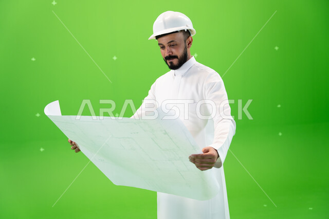 Developing and developing the Saudi engineering field, looking at the construction plan, portrait of a Saudi Gulf Arab engineer wearing the traditional dress and a protective hat at the work site, the concept of engineering and construction work, Saudi pr