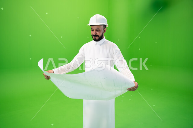 Developing and developing the Saudi engineering field, looking at the construction plan, portrait of a Saudi Gulf Arab engineer wearing the traditional dress and a protective hat at the work site, the concept of engineering and construction work, Saudi pr