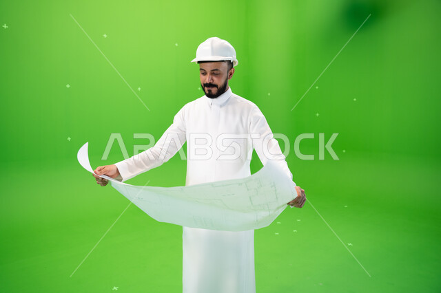 النظر إلى مخطط الإنشاءات, بورتريه لمهندس عربي خليجي سعودي يرتدي الثوب التقليدي وقبعة الحماية في موقع العمل, مفهوم الهندسة وأعمال البناء, مهن ووظائف سعودية,  تنمية وتطوير المجال الهندسي السعودي, متابعة الأعمال الهندسية, خلفية خضراء, كروما