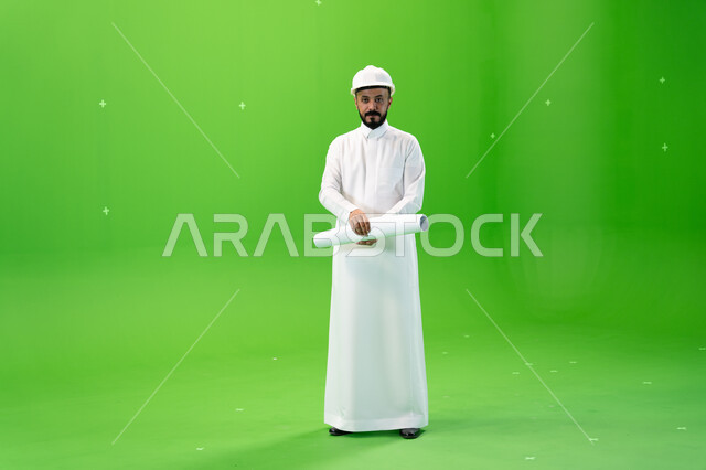 Ambition at work to achieve success, standing with gestures of confidence and developing the engineering field, portrait of a Saudi Arabian Gulf engineer wearing traditional dress and protective hat standing at the work site, full length body image, green