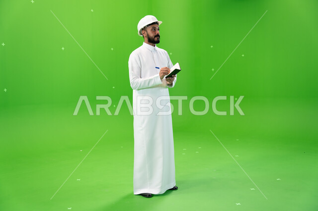  العمل في القطاع الهندسي السعودي, مهن ووظائف سعودية, بورتريه لمهندس عربي خليجي سعودي يرتدي قبعة الحماية يقف في موقع العمل, تسجيل وتدوين ملاحظات البناء والإنشاءات, الإعمار بسواعد أبناء الوطن, صورة الجسم بالطول الكامل, خلفية خضراء, كروما