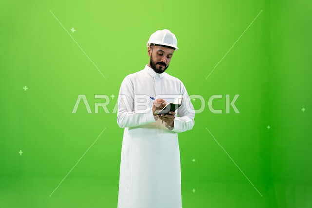 Recording and recording building and construction notes, Saudi professions and jobs, working in the Saudi engineering sector, a portrait of a Saudi Arab Gulf engineer wearing a protection hat standing at the work site, reconstruction by the hands of the p