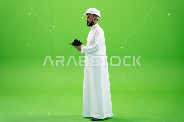 الإعمار بسواعد أبناء الوطن, مهن ووظائف سعودية, العمل في القطاع الهندسي السعودي, بورتريه من الجانب لمهندس عربي خليجي سعودي يرتدي قبعة الحماية يقف في موقع العمل, تسجيل وتدوين ملاحظات البناء والإنشاءات, صورة الجسم بالطول الكامل, خلفية خضراء, كروما