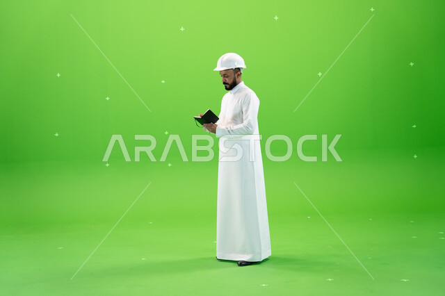 وظائف ومهن سعودية, العمل في القطاع الهندسي السعودي, بورتريه لمهندس عربي خليجي سعودي يرتدي قبعة الحماية يقف في موقع العمل, تسجيل وتدوين ملاحظات البناء والإنشاءات, الإعمار بسواعد أبناء الوطن, صورة الجسم بالطول الكامل, خلفية خضراء, كروما