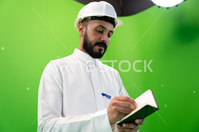 مهن ووظائف سعودية, العمل في القطاع الهندسي السعودي, بورتريه مقرب لمهندس عربي خليجي سعودي يرتدي قبعة الحماية يقف في موقع العمل, تسجيل وتدوين ملاحظات البناء والإنشاءات, الإعمار بسواعد أبناء الوطن, خلفية خضراء, كروما