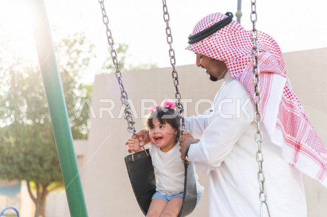فتاه جميلة مصابة بملازمة داون تقضي وقتها في نزهه مع والدها بالمنتزه ، اب سعودي خليجي يأرجح ابنته على  لعبة الارجوحة ، أصحاب الهمم ، ذوي الاحتياجات الخاصة
