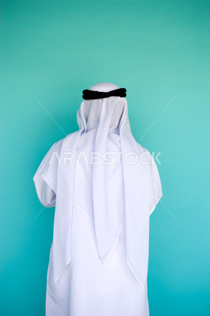 الاهتمام بالمظهر الخارجي, الوقوف باستقامة وثقة, بورتريه من الخلف لرجل عربي خليجي امارتي يرتدي الكندورة والغترة الاماراتية , خلفية زرقاء