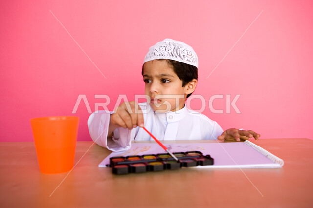 Developing artistic skills in Emirati kindergartens, a portrait of an Arab Gulf Emirati child wearing traditional Emirati clothing, drawing and coloring with watercolours, the concept of interest in hobbies, pink background