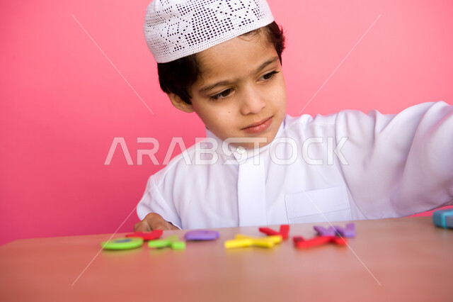 Using and recognizing the forms of English letters, learning skill through educational games, a close-up portrait of an Arab Gulf Emirati child wearing Emirati clothes and playing with the alphabet puzzle game, enjoying useful recreational activities, col