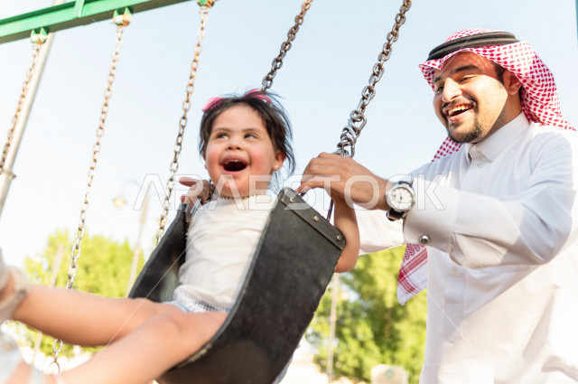 فتاه جميلة مصابة بملازمة داون تقضي وقتها في نزهه مع والدها بالمنتزه ، اب سعودي خليجي يأرجح ابنته على  لعبة الارجوحة ، أصحاب الهمم ، ذوي الاحتياجات الخاصة