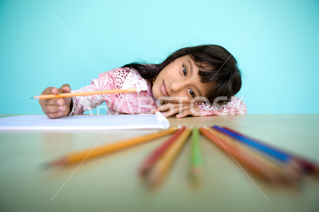 رعاية المواهب والاهتمام بها في الإمارات العربية المتحدة, تطوير وتنمية الهوايات, النظر الى الكاميرا، أدوات وقرطاسية التلوين، بورتريه مقرب لفتاة صغيرة عربية خليجية إماراتية تقوم بالرسم والتلوين بالأقلام الخشبية، خلفية زرقاء