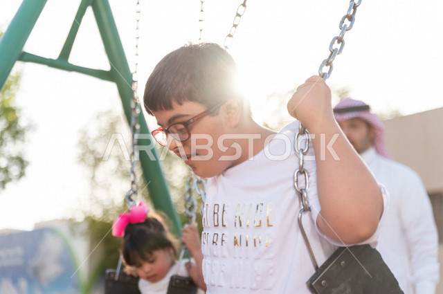 ولد سعوي خليجي مصاب بملازمة داون يقضي وقته في نزهه مع والده  بالمنتزه ، يستمتع باللعاب على الارجوحة ، أصحاب الهمم ، ذوي الاحتياجات الخاصة