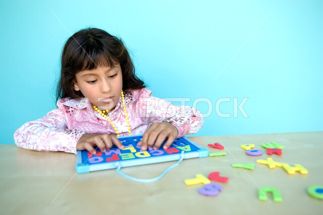 التعلم عن طريق الألعاب التثقيفية، استثمار أوقات الفراغ بالأشياء المفيدة, التسلية والترفيه بالأنشطة التعليمية, التعرف على أشكال الحروف الأجنبية، بورتريه مقرب لفتاة عربية خليجية إماراتية تقوم بحل لغز الأبجدية , خلفية زرقاء