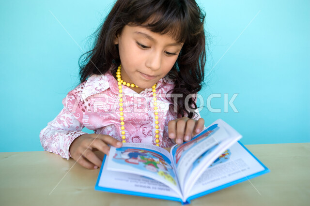 تمضية أوقات الفراغ بالتعلم والتثقف الذاتي, إيماءات الانتباه والتركيز بالمطالعة, بورتريه مقرب لفتاة عربية خليجية إماراتية تقوم بالقراءة بتمعن , مطالعة القصص التصويرية المسلية, تنمية مهارات القراءة للأطفال, الاهتمام بتصفح الكتب المفيدة, خلفية زرقاء