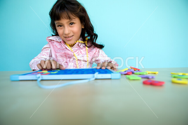 التعلم عن طريق الألعاب التثقيفية، استثمار أوقات الفراغ بالأشياء المفيدة, التسلية والترفيه بالأنشطة التعليمية, التعرف على أشكال الحروف الأجنبية، بورتريه مقرب لفتاة عربية خليجية إماراتية تقوم بحل لغز الأبجدية , خلفية زرقاء