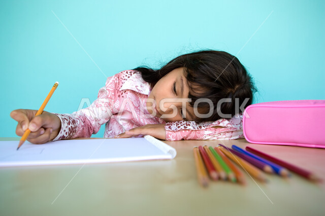 إيماءات الاندماج والتركيز في الأنشطة الفنية، تطوير وتنمية الهوايات, أدوات وقرطاسية التلوين، بورتريه مقرب لفتاة صغيرة عربية خليجية إماراتية تقوم بالرسم والتلوين بالأقلام الخشبية، رعاية المواهب والاهتمام بها في الإمارات العربية المتحدة, خلفية زرقاء