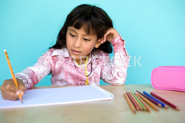 Gestures of integration and focus in artistic activities, development and development of hobbies, coloring tools and stationery, close-up portrait of a young Arab Gulf Emirati girl drawing and coloring with wooden pens, nurturing and caring for talents in