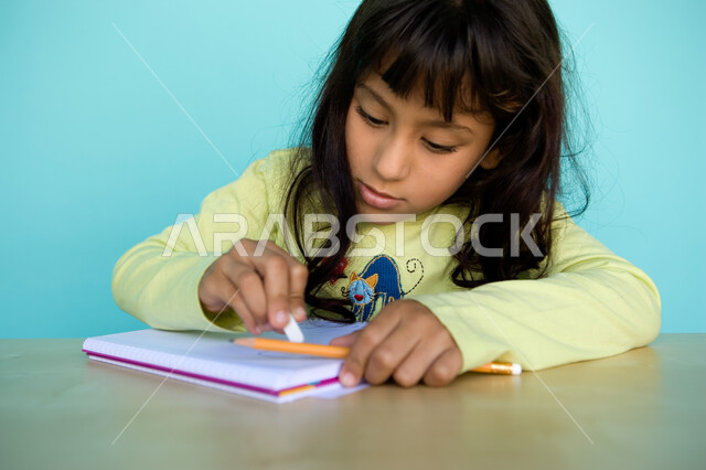 Developing and cultivating hobbies, gestures of integration and focus in artistic activities, drawing with a pencil, a close-up portrait of a young Arab Gulf Emirati girl erasing the drawing with an eraser, nurturing and caring for talents in the United A