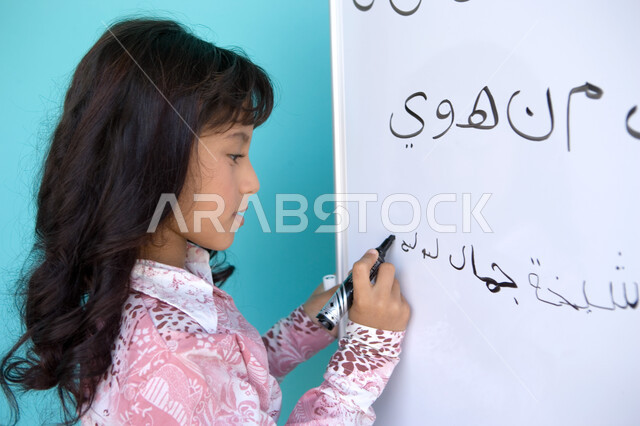 Developing the linguistic and intellectual abilities of students, teaching students to form words in the Arabic language, the quality of education in the Emirates, a close-up portrait from the side of an Arab Gulf Emirati girl holding a blackboard pen in 