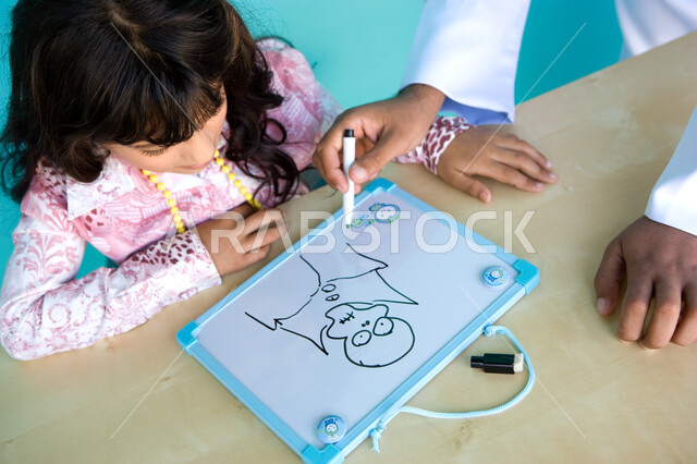 Paying attention to and nurturing children’s talents, the role of parents in developing artistic skills, gestures of happiness and enjoyment of sharing artistic activities with the father, passion and love of drawing, close-up portrait of a young Arab Gul