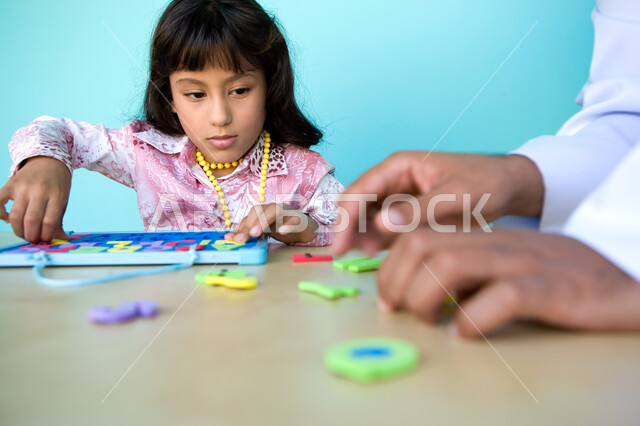 التسلية والترفيه بالأنشطة التعليمية, الاهتمام بتعليم وترفيه الأبناء, التعلم عن طريق الألعاب التثقيفية، التعرف على أشكال الحروف الأجنبية، بورتريه مقرب لفتاة عربية خليجية إماراتية تقوم بحل لغز الأبجدية بمساعدة والدها , خلفية زرقاء