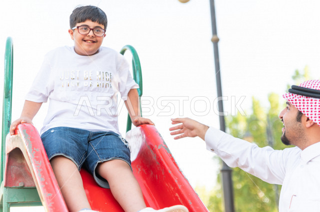ولد سعوي خليجي مصاب بملازمة داون يقضي وقته في نزهه مع والده  بالمنتزه ، يستمتع باللعاب على الارجوحة ، أصحاب الهمم ، ذوي الاحتياجات الخاصة