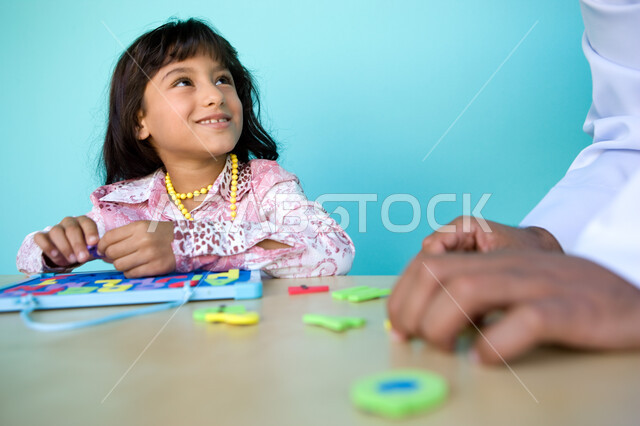 الاهتمام بتعليم وترفيه الأبناء, التسلية والترفيه بالأنشطة التعليمية, التعلم عن طريق الألعاب التثقيفية، التعرف على أشكال الحروف الأجنبية، بورتريه مقرب لفتاة عربية خليجية إماراتية تقوم بحل لغز الأبجدية بمساعدة والدها وتنظر اليه بإيماءات الحب , خلفية زرقاء