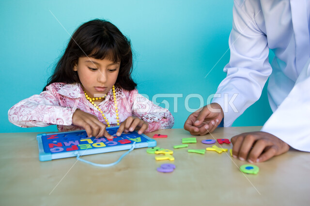 Interest in educating and entertaining children, entertainment and entertainment with educational activities, learning through educational games, recognizing the shapes of foreign letters, a close-up portrait of an Arab-Gulf-Emirati girl solving the puzzl